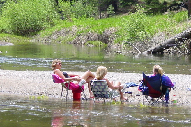Three women in lawn chairs sitting in the shallow Stanislaus River at the Kegger Backpack campsite