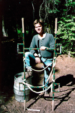 The blue steel stretcher leaning against a fence — rope-wrapped handles, cargo straps, current version